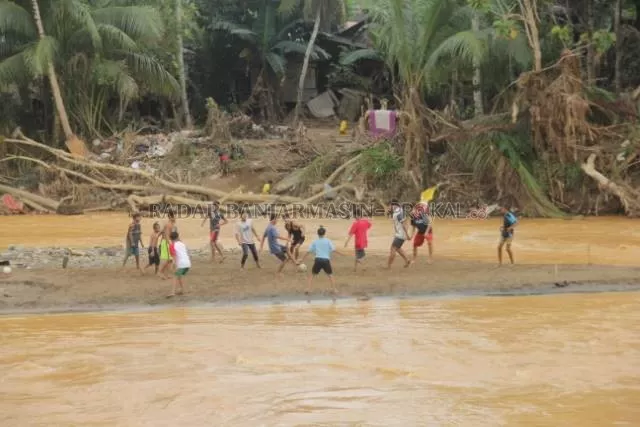 TETAP CERIA: Anak-anak di Desa Waki, Hulu Sungai Tengah bermain bola dilatar-belakangi kerusakan yang ditinggalkan akibat banjir bandang. Banjir bandang yang melanda Desa mereka 14 Januari lalu membuat rumah-rumah hancur. | FOTO: JAMALUDIN/RADAR BANJARMASIN