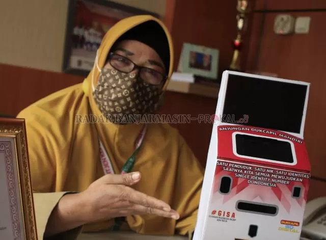 MAHAL: Kepala Disdukcapil Kota Banjarbaru, Sri Fatma K menunjukkan miniatur mesin ADM. | Foto: Muhammad Rifani/Radar Banjarmasin