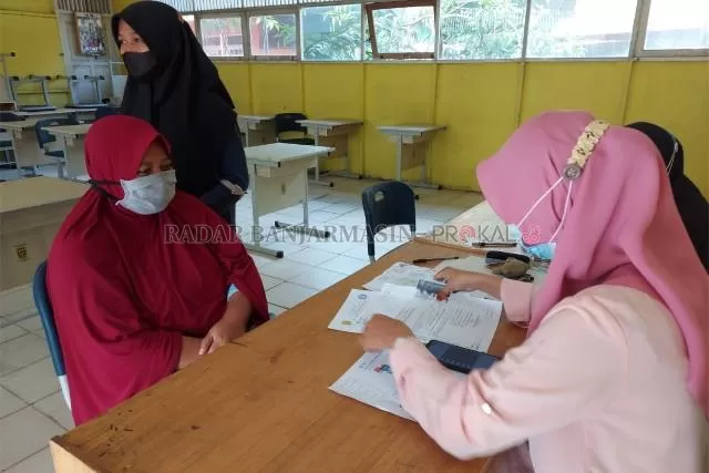 SEMI DARING: Petugas PPDB di SMPN 33 Banjarmasin mendampingi orang tua murid yang kesulitan mendaftar secara daring. | FOTO: WAHYU RAMADHAN/RADAR BANJARMASIN