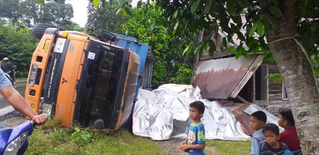 TERBALIK : Kondisi truk angkutan semen yang terbalik di Desa Sei Pimping menyebabkan kerusakan rumah warga.