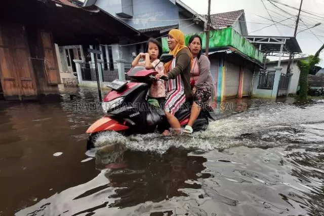 TEROBOS BANJIR: Warga Jalan Prona di Banjarmasin Selatan, menerobos banjir yang merendam jalan dan permukiman. | FOTO: WAHYU RAMADHAN/RADAR BANJARMASIN