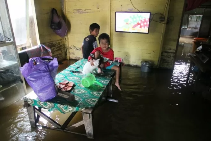 TERKEPUNG BANJIR: Anak-anak di Teluk Selong menonton televisi dari atas meja makan. | FOTO: BPBD BANJAR FOR RADAR BANJARMASIN