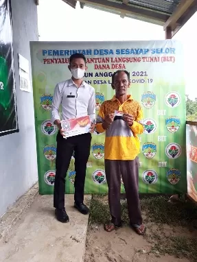 SIMBOLIS: Plt Kepala Desa Sesayap Selor Indra Hatari saat memberikan kartu BLT untuk memudahkan warga penerima PKM, Rabu (7/4).
 RIKO / RADAR TARAKAN