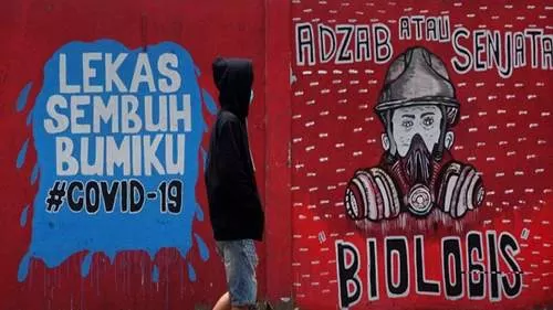 Pemuda mengenakan masker berjalan melewati mural di tengah kekhawatiran wabah Corona yang sudah menyebar di seluruh Indonesia. (FAJRIN RAHARJO/AFP)
