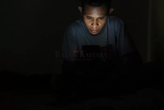 LISTRIK PADAM: Tinus, warga Jalan Cendana saat bekerja melalui telepon pintar di tengah kegelapan saat PLN memadamkan listrik menyeluruh di Tanjung Selor, Senin (28/9) malam.