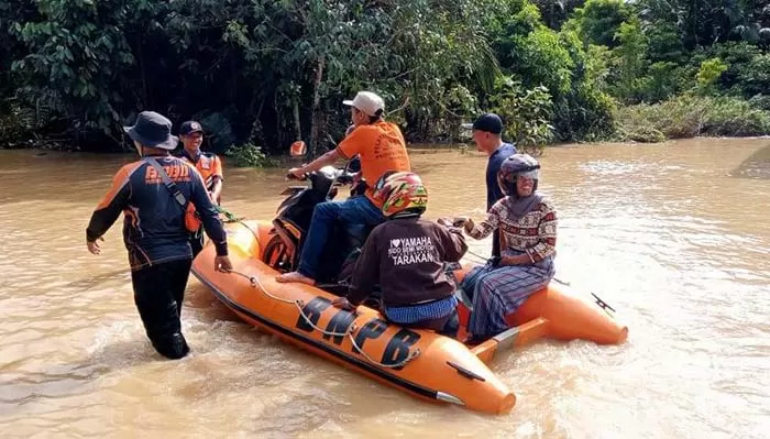 RENDAM RUAS JALAN: Personel BPBD Kaltara bersama BPBD Nunukan membantu warga yang melintas di jalan poros terdampak banjir.