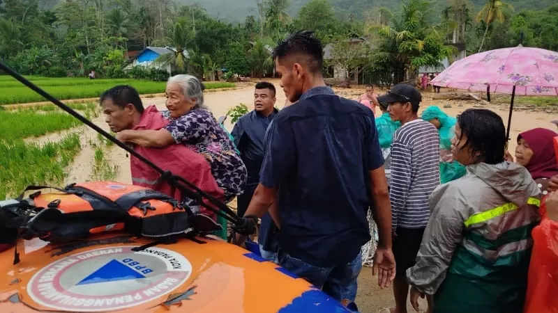 Hujan deras yang terjadi tiba-tiba di Kota Padang pada Sabtu (31/1/2026) sore membuat kawasan Pasa Lalang, Kecamatan Kuranji dilanda limpahan air sungai. Terlihat petugas BPBD mengevakuasi seorang wanita lanjut usia (lansia) ke area lebih aman. (Dok. Pusdalops PB)