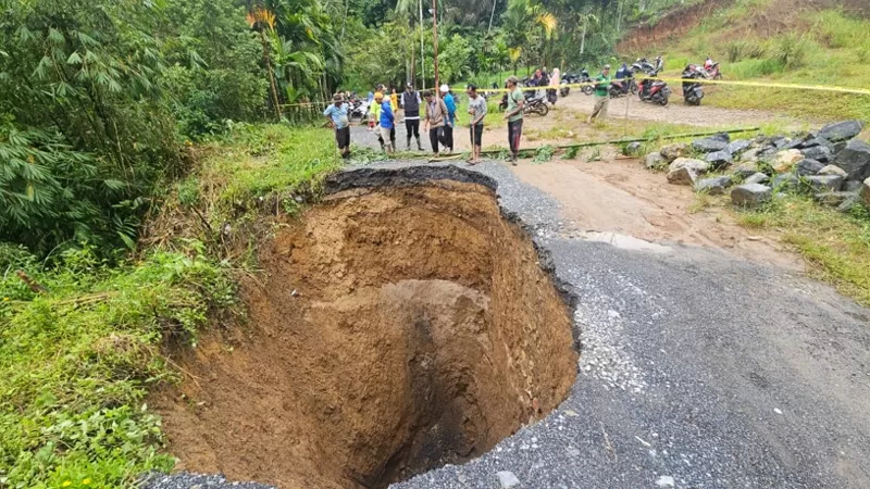Warga dan aparat meninjau ruas jalan kabupaten di Nagari Situjuah Ladang Laweh, Kabupaten Limapuluh Kota, Sumatera Barat, yang amblas menyerupai sinkhole dan tertimbun material longsor akibat hujan deras, Rabu (13/5/2026) pagi. (Dok. Istimewa)