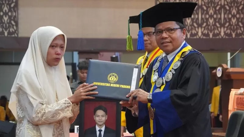 Foto Rendi Kurniawan memegang foto putranya saat prosesi wisuda, setelah Rendi dinyatakan lulus dari Program Studi S1 Pendidikan Matematika FMIPA UNP dengan IPK 3,71. Selasa (25/8/2026). (Foto: UNP)
