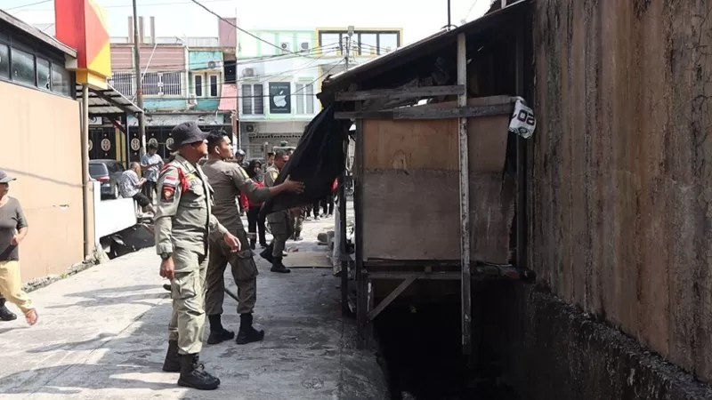 Personel Pleton Dalmas dan tim khusus Satpol PP Kota Padang membantu proses pembongkaran dan pemindahan bangunan liar yang memanfaatkan fasilitas drainase di kawasan Jalan HOS Cokroaminoto, samping Kakiku, Kelurahan Berok Nipah, Kecamatan Padang Barat pada Sabtu (22/8/2026) siang. (Dok. Humas)