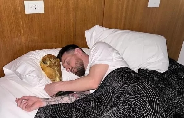 Ilustrasi Messi tidur dengan trofi Piala Dunia - suratdokter.com
