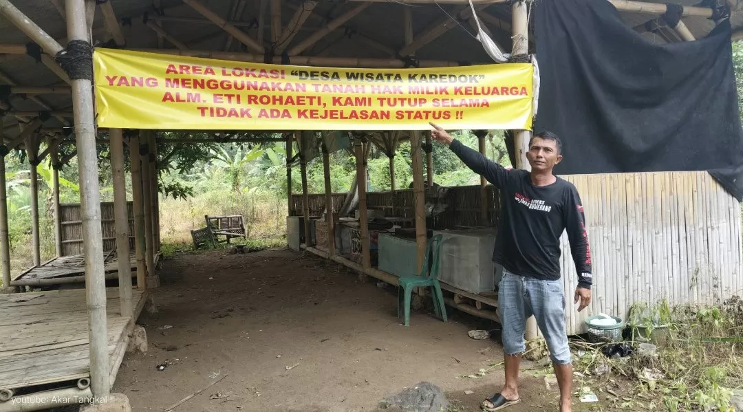 Foto : Akup Jaenal, berdiri menunjuk baligo penyegelan tanah di lokasi Desa Wisata Karedok, Rabu (11/02/2026) Siang. - G'jodt