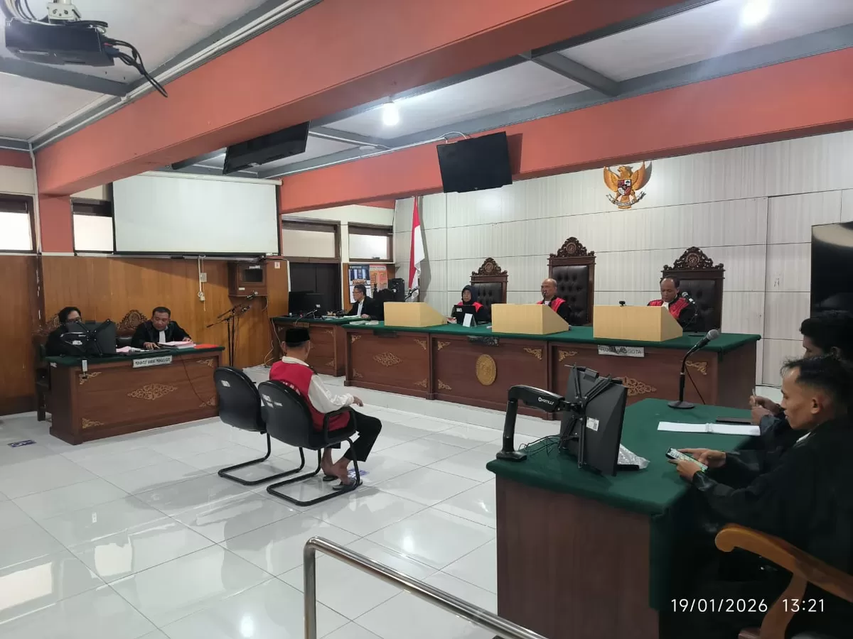 Simbol Keadilan: Timbangan keadilan diletakkan di atas kitab undang-undang, melambangkan proses peradilan yang sedang berlangsung.