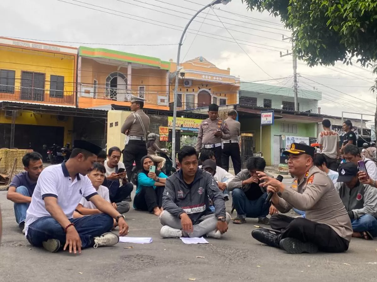 Kapolres Bulukumba AKBP Restu Wijayanto memilih duduk lesehan di atas aspal bersama massa Aliansi Pemuda Sapobonto saat menerima aksi unjuk rasa terkait kasus pencurian sapi dan pelarian terduga pelaku di depan Mapolres Bulukumba, Senin (27/04/2026).