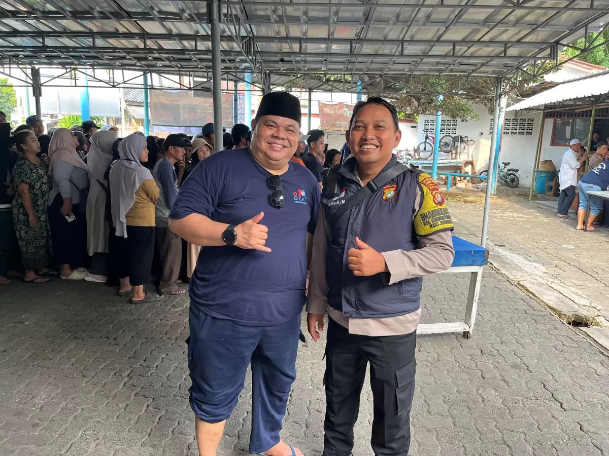 Bhabinkamtibmas Gunung Sahari Utara Aipda Adnan Munandar bersama Ketua Pelaksana Adam Noviar memantau jalannya pembagian daging kurban agar tetap kondusif. (WartaPesona.com)
