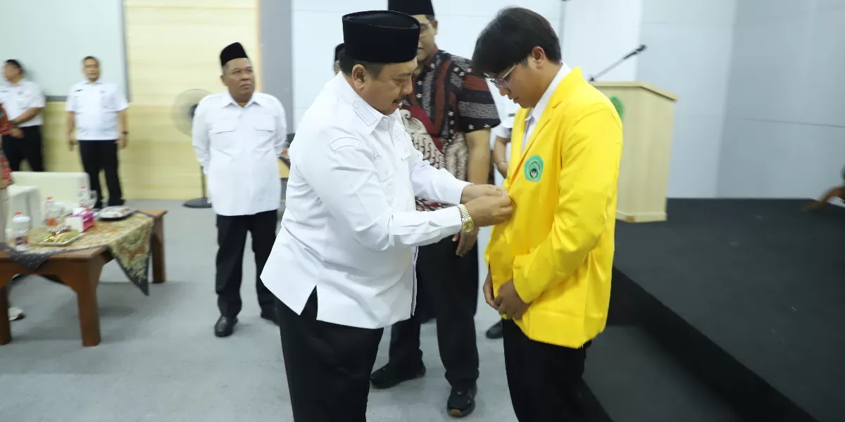 Penyerahan secara simbolis dilakukan Bupati Jombang Warsubi, melalui pemakaian jas almamater Undar kepada salah satu mahasiswa penerima beasiswa (jombangkab.go.id)