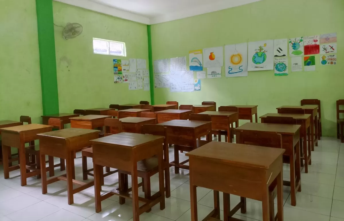 Haikal berdiri di teras ruang kelas memperlihatkan bangunan sekolah yang selesai direnovasi dan dicat rapi.