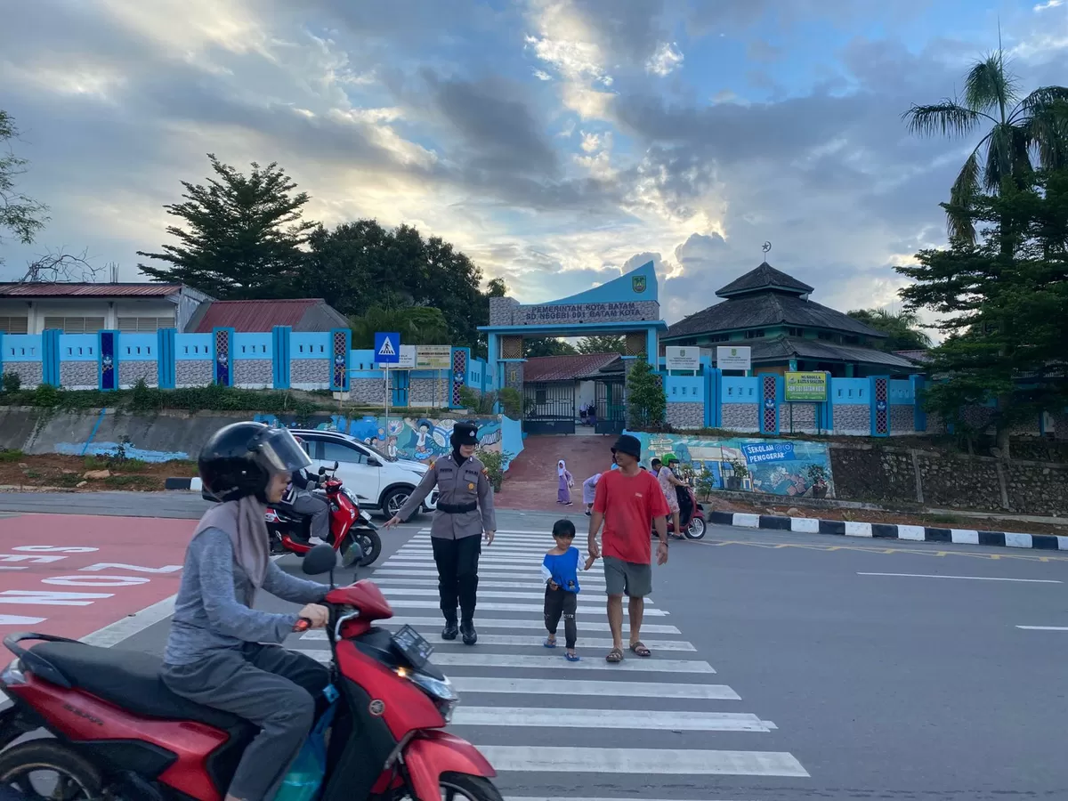 Polwan membantu anak-anak menyeberangi jalan raya, serta mengatur arus kendaraan yang datang dan pergi di SDN 001 Batam Kota. (Humas Polresta Barelang)