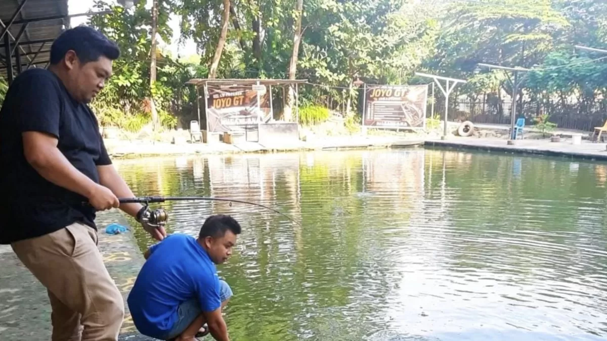 Seorang pengunjung Kolam Pancing GT, Gilang saat menjajal sensasi tarikan kolam Galatama, di bantu Chandro pengelola. (Muhammad Kamil.)