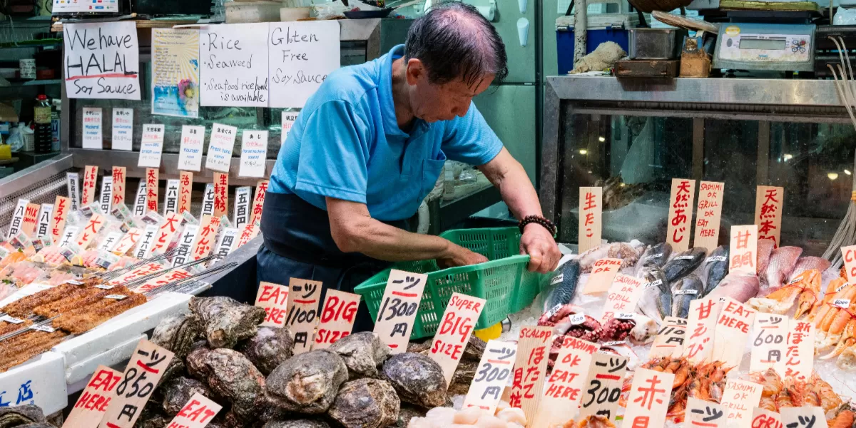 Seorang penjual sedang menata makanan laut segar di sebuah kios pasar Jepang yang ramai dengan berbagai papan tanda, termasuk halal. Saat kamu akan mulai berbisnis terutama makanan segera urus sertifikasi halal agar konsumen tidak ragu untuk membeli makanan. (Pexels @Emanuele Ricciardi)