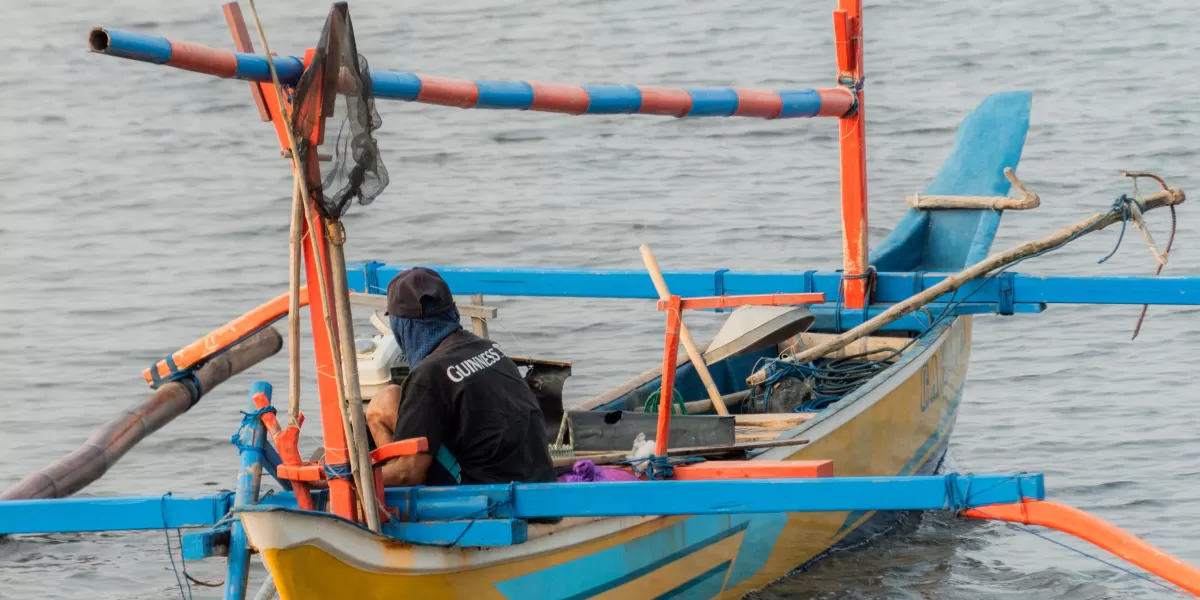 Seorang nelayan mempersiapkan perlengkapan melaut di perahu tradisional yang berwarna cerah di perairan Indonesia yang tenang. (Pexels @Muhammad Bahauddin)