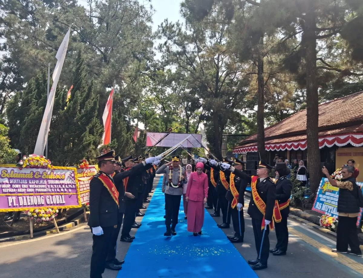 Kapolres Subang AKBP Andi Purwanto bersama Ketua Bhayangkari Cabang Subang, Ny. Echi Andi, berjalan di bawah lengkung pedang dalam prosesi Tradisi Pedang Pora saat penyambutan di Mapolres Subang, Rabu 29 Juli 2026