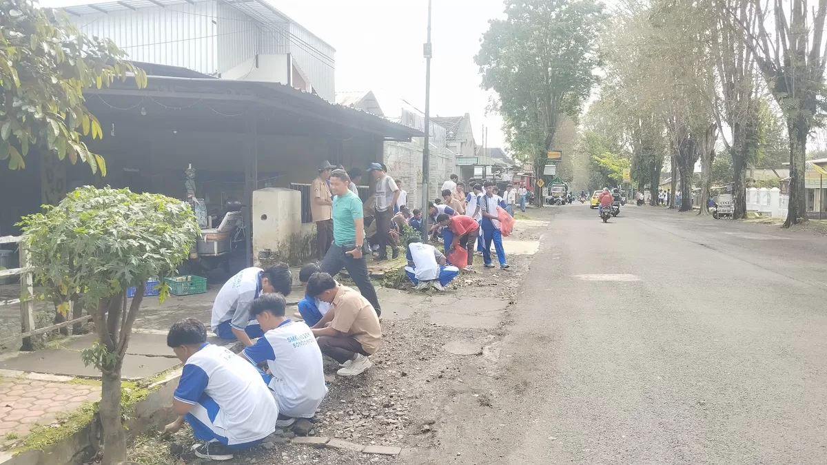 Puluhan siswa SMKN 3 Bondowoso tampak sedang membersihkan badan Jalan Santawi. (SketsaNusantara.id)