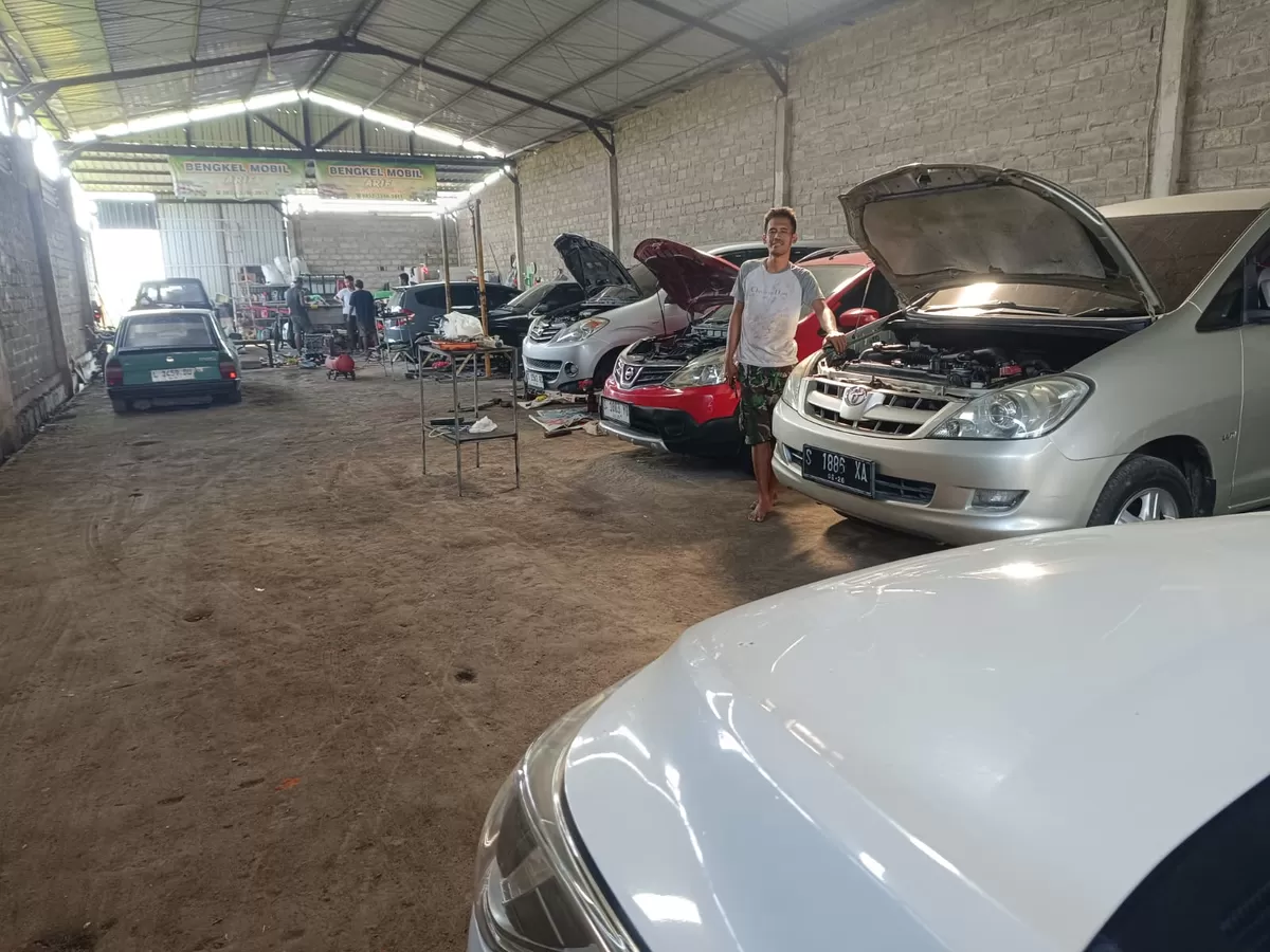 Arif Choirudin berdiri di antara mobil-mobil di bengkelnya. (SketsaNusantara.id/As'ad Choirudin)