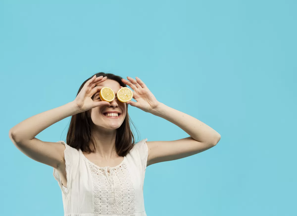 Ilusrasi seorang wanita tersenyum sambil memegang jeruk lemon yang ditaruh di kedua matanya. (Freepik)