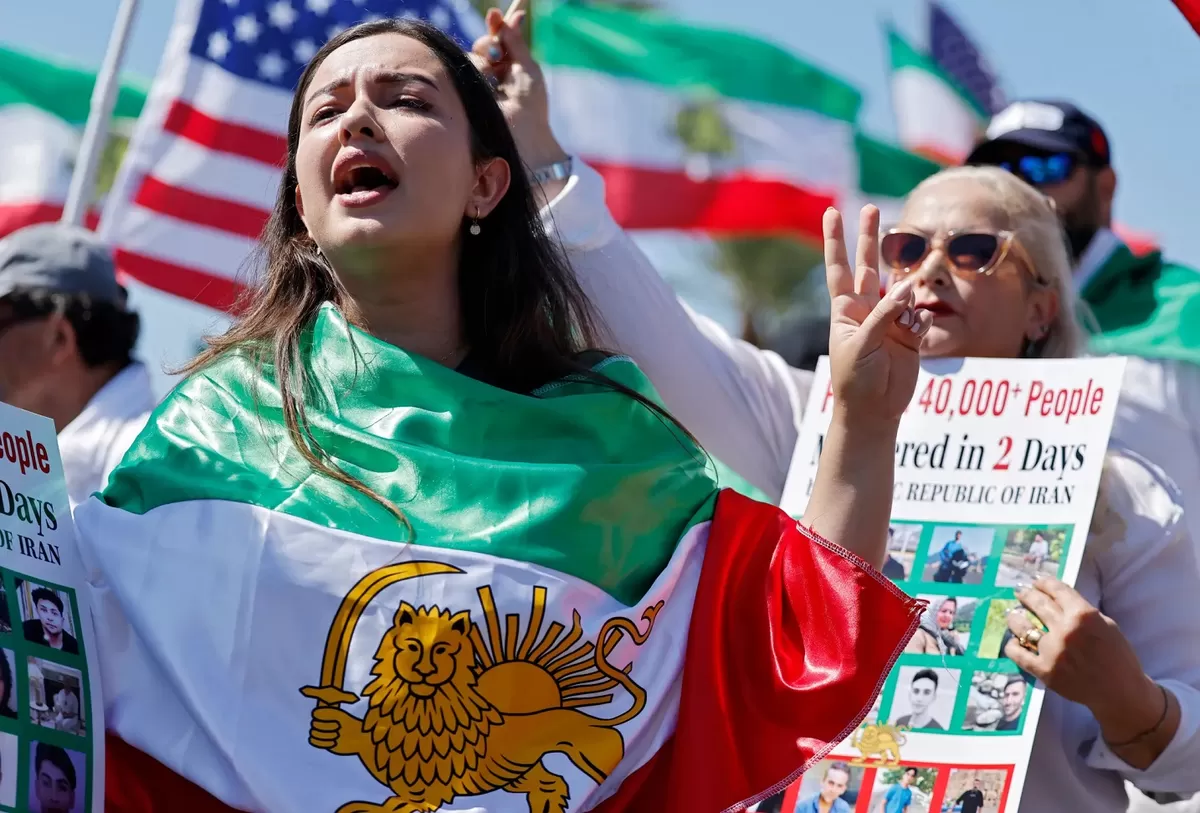 Seorang demonstran berunjuk rasa menentang Republik Islam Iran sambil mengenakan bendera Iran pra-revolusi di luar Stadion Los Angeles.