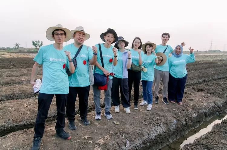 Hening Parlan, Director of GreenFaith Indonesia, together with the Team from GreenFaith Japan led by Yoshiro Sada, Director of Green Faith Japan, are on a stretch of agricultural land with the PLTU Indramayu I building in the background.