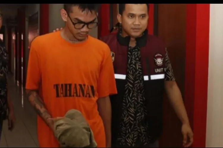 Seleb TikTok Satria Mahathir 'Cogil' ditahan polisi terkait pengeroyokan. Penampilannya dalam baju tahanan menciptakan sorotan dalam konferensi pers di Polresta Barelang.