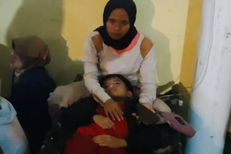 Seorang ibu memeluk anaknya di puskesmas setelah sang anak dirawat akibat keracunan makanan program makan gratis.