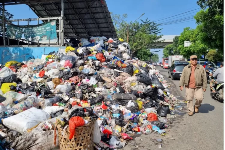 Warga melintasi tumpukan sampah di TPS Pasar Rahayu, baru -batu ini