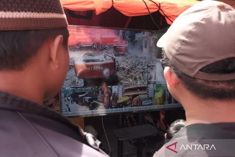 Warga melihat proses evakuasi jenazah korban Ponpes Al Khoziny melalui sambungan langsung yang difasilitasi oleh Pemkab Sidoarjo, Minggu (5/10/2025).  (ANTARA/Fahmi Alfian)