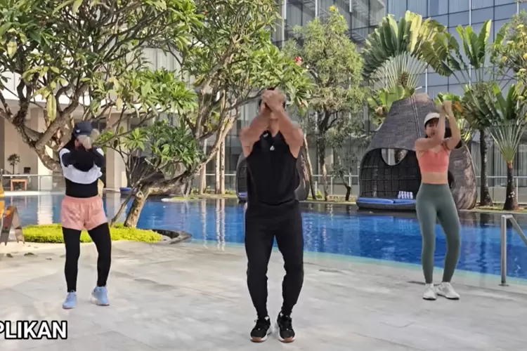Gambar ini memperlihatkan tiga orang melakukan senam di area tepi kolam renang, dikelilingi pepohonan dan bangunan modern. Aktivitas ini termasuk olahraga ringan yang bermanfaat untuk menjaga kebugaran dan meningkatkan suasana hati. (Foto/YouTube - @BodyFitByBagus.)
