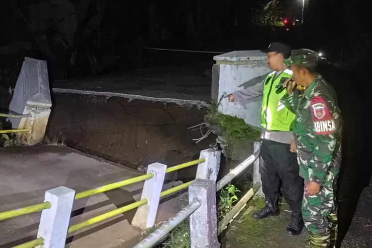 Polisi menunjuk jembatan yang ambles akibat terkikis dan tergerus aliran sungai dibawahnya.  (Dokumen)