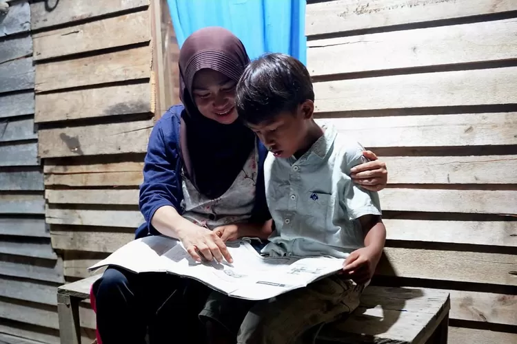 Wiwik Handayani (kiri), warga Sungai Kunyit, Mempawah, Kalimantan Barat sedang menemani anaknya belajar di rumah saat malam hari pasca menerima bantuan penyambungan listrik gratis melalui program Light Up The Dream PLN. (ISTIMEWA)