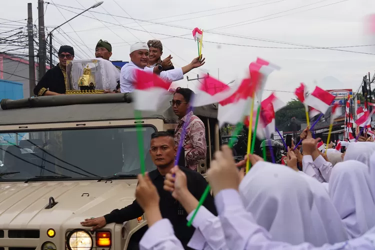 Bupati Bogor Rudy Susmanto dan Radya Anom Luky Djohari Soemawilaga menyapa pelajar yang menyambut Kirab Mahkota Binokasih di Jalan Raya Karadenan - Sukahati, Cibinong, Kabupaten Bogor, Senin, 21 April 2025. (Arifin - Metropolitan)