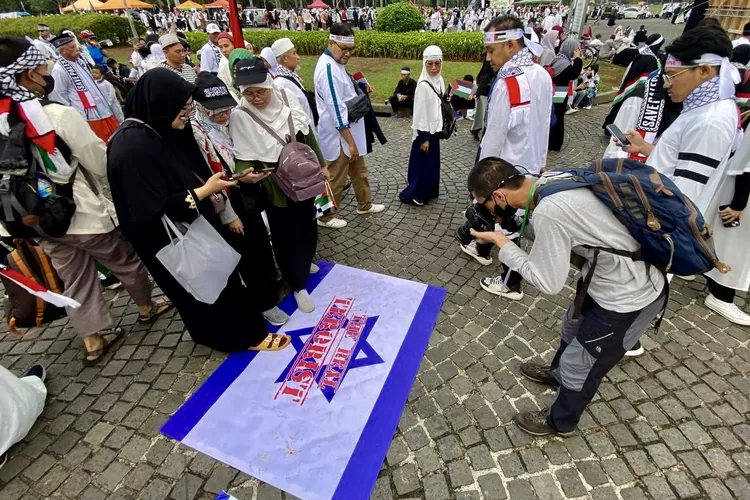 Seorang pewarta foto tengah mengabadikan massa aksi bela Palestina di Monas menginjak-injak bendera Israel - Foto: Henry Lukmanul Hakim