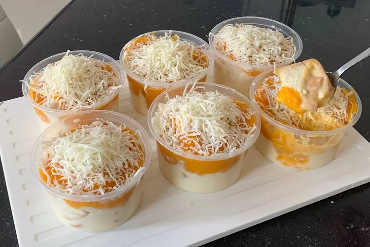 Puding mangga keju lembut dengan lapisan warna cerah, dihias daun mint untuk sentuhan elegan