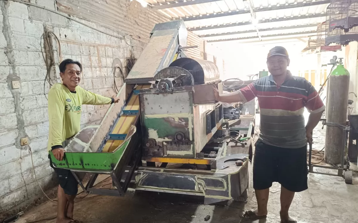 Misbachul Munir (kiri) bersama karyawan menunjukkan mesin konveyor perontok jagung hasil produksinya. (SketsaNusantara.id/As'ad Choirudin)