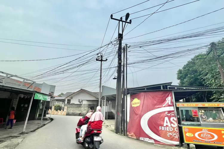 BERBAHAYA : Seorang pengendara saat melintas yang tepat di atasnya terdapat kabel berantakan yang melintang di Jalan Rivaria Dalam, Kelurahan Bedahan, Kecamatan Sawangan, Rabu (12/2) (RISKY DWI LESTARI/RADAR DEPOK)