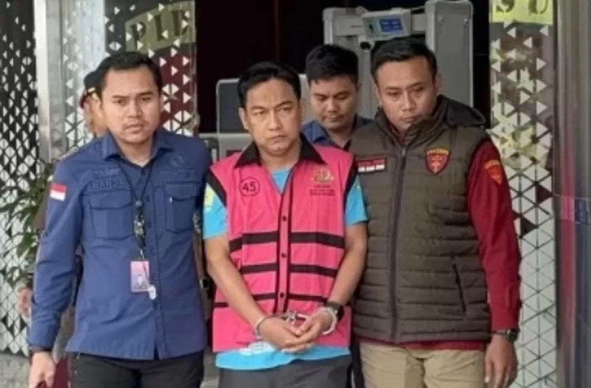 Ketua Ombudsman Hery Susanto memakai jaket pink bergaris sambil diborgol dikawal dua penyidik.
