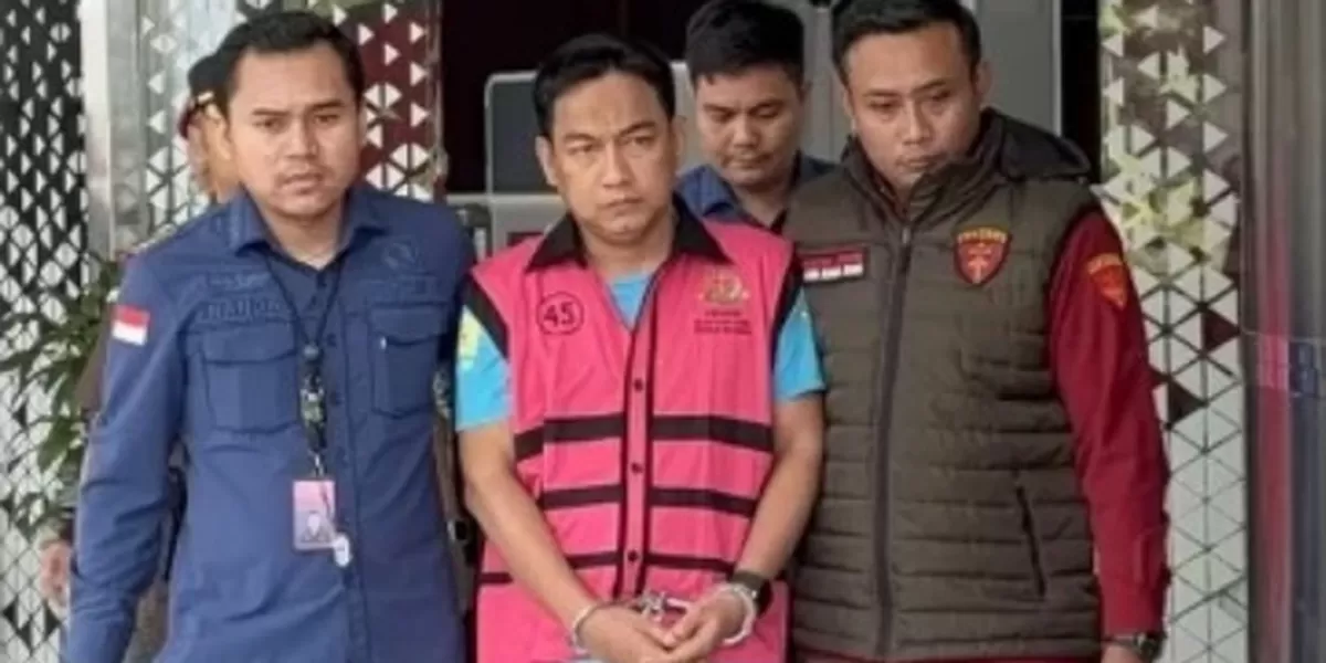 Ketua Ombudsman Hery Susanto memakai jaket pink bergaris sambil diborgol dikawal dua penyidik.